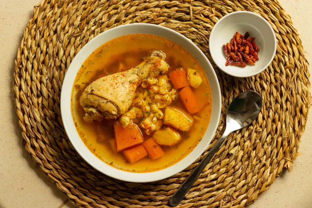 Sancocho de gallina de patio servido en tazón de barro, con maíz, papa y zanahoria